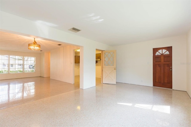 empty room with visible vents, a notable chandelier, and speckled floor