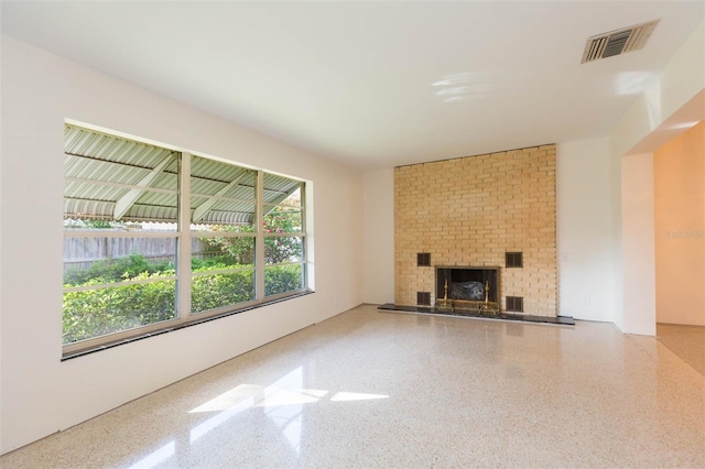 unfurnished living room featuring a brick fireplace, visible vents, and speckled floor