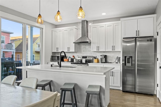 kitchen with a breakfast bar area, stainless steel appliances, light countertops, wall chimney range hood, and tasteful backsplash