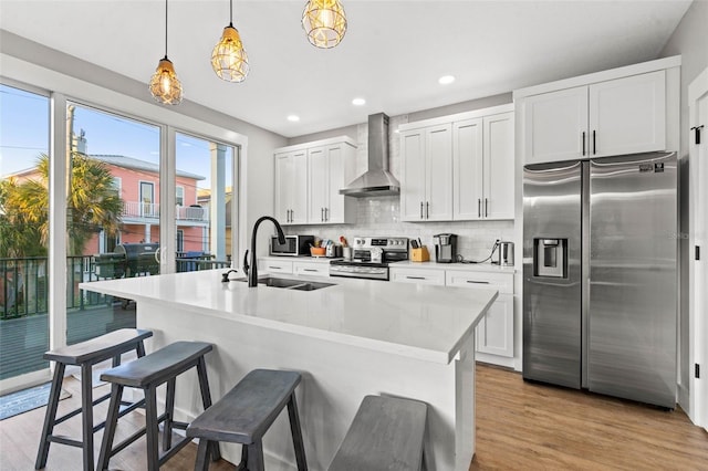 kitchen featuring stainless steel appliances, tasteful backsplash, a sink, wall chimney range hood, and a kitchen bar