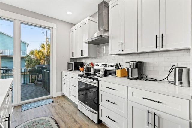 kitchen with light wood finished floors, white cabinets, wall chimney exhaust hood, stainless steel appliances, and light countertops