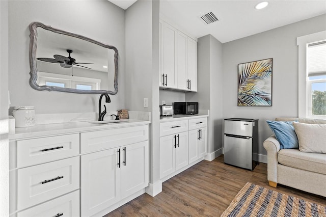 bar featuring black microwave, wood finished floors, a sink, and visible vents