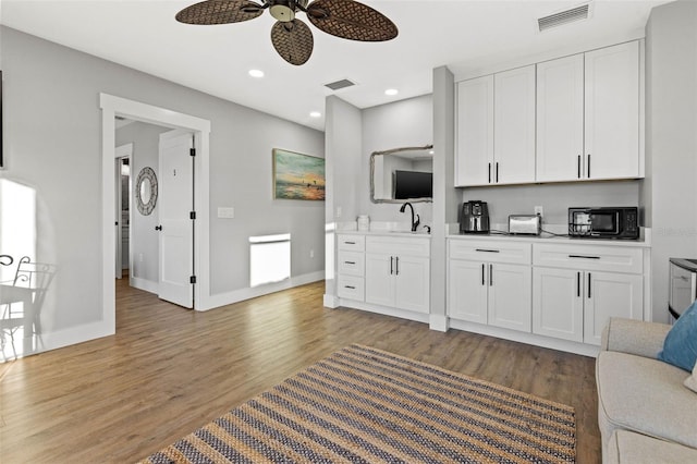 kitchen featuring black microwave, light wood-type flooring, visible vents, and white cabinetry