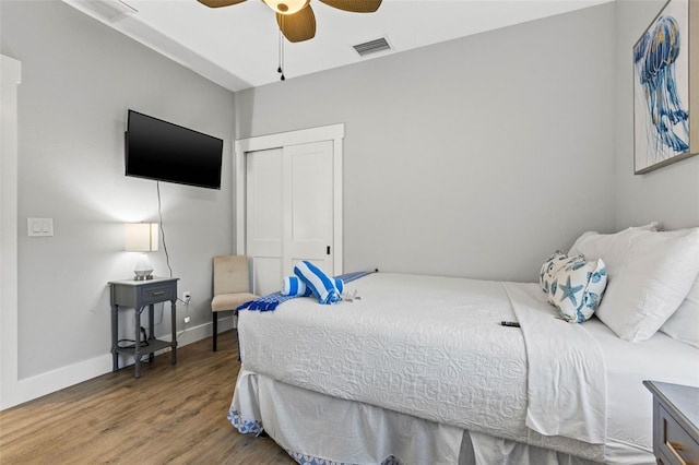 bedroom with baseboards, visible vents, ceiling fan, wood finished floors, and a closet