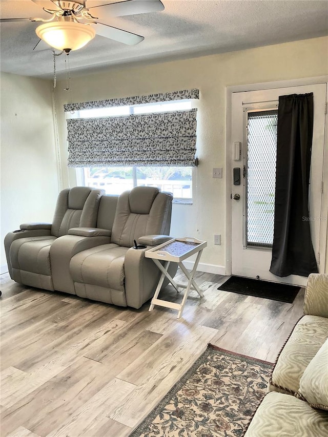 living area featuring light wood finished floors, baseboards, a textured ceiling, and a ceiling fan