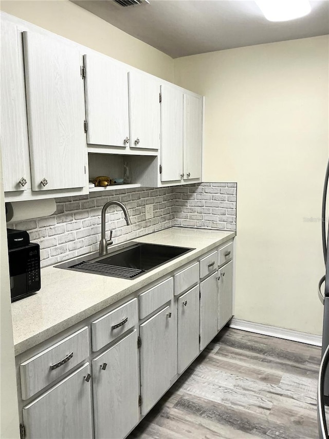 kitchen with visible vents, light wood-type flooring, light countertops, decorative backsplash, and a sink