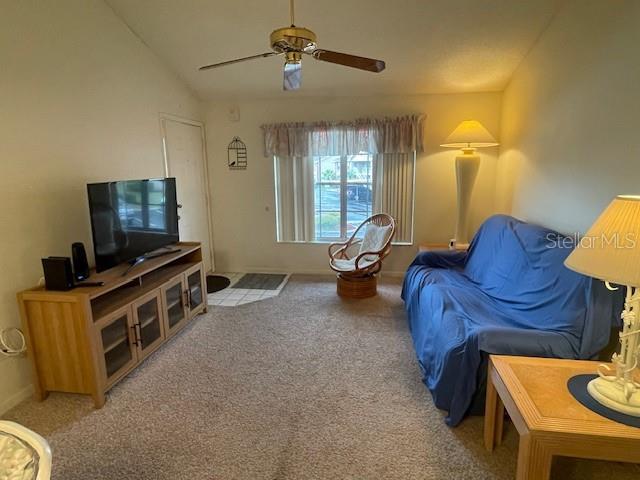 living room featuring light carpet, baseboards, a ceiling fan, and lofted ceiling