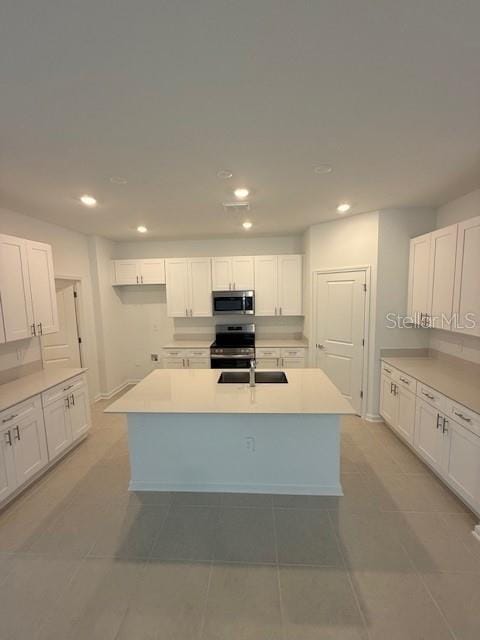 kitchen with appliances with stainless steel finishes, recessed lighting, white cabinetry, and an island with sink