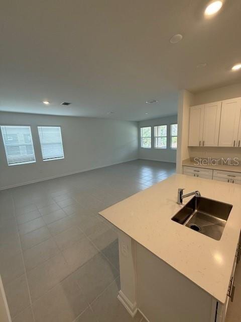 kitchen featuring a kitchen island, a sink, white cabinets, open floor plan, and light countertops