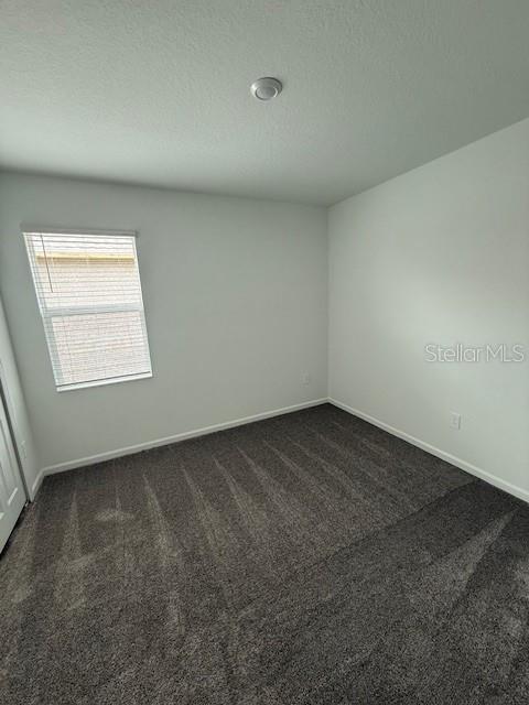 unfurnished room featuring a textured ceiling, dark carpet, and baseboards