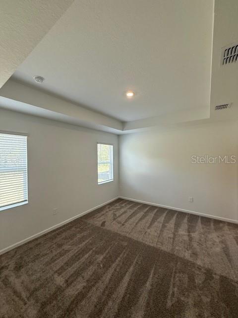 empty room featuring a tray ceiling, carpet, visible vents, and baseboards