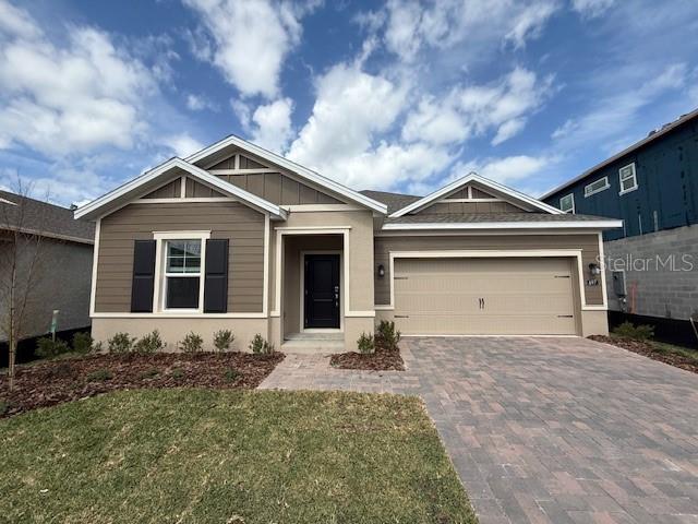 view of front of property featuring a garage, decorative driveway, a front lawn, and board and batten siding