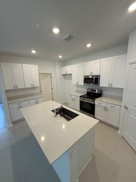 kitchen featuring recessed lighting, stainless steel appliances, a sink, white cabinetry, and light countertops