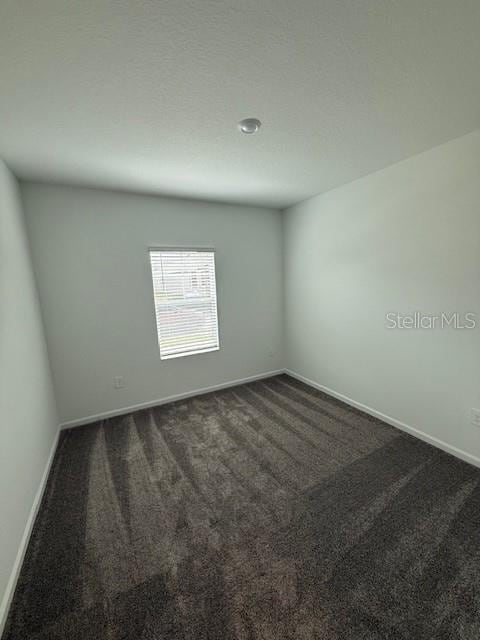 unfurnished room with dark colored carpet and baseboards