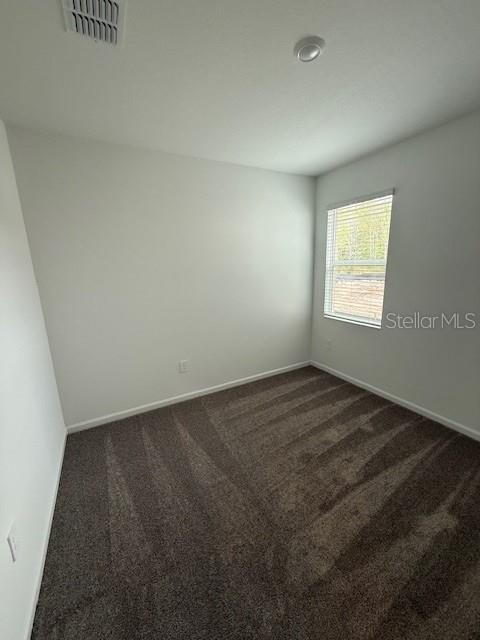 spare room with dark carpet, visible vents, and baseboards