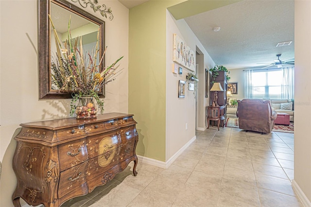 hallway with tile patterned floors, a textured ceiling, and baseboards