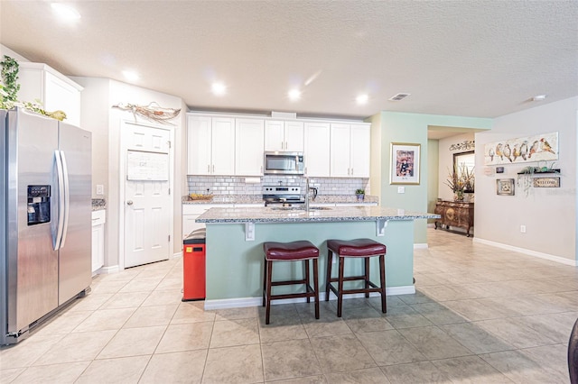 kitchen featuring visible vents, a kitchen island with sink, backsplash, white cabinetry, and stainless steel appliances