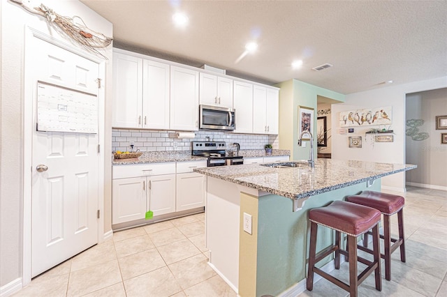 kitchen with visible vents, a sink, a kitchen breakfast bar, white cabinetry, and appliances with stainless steel finishes