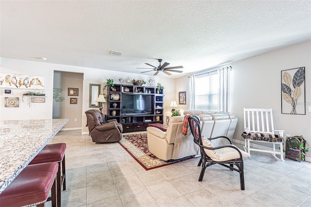 living area featuring light tile patterned floors, visible vents, a textured ceiling, and ceiling fan