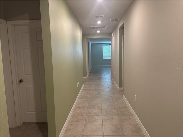 hallway featuring light tile patterned floors, baseboards, and visible vents