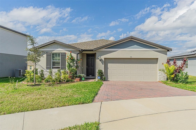 ranch-style home featuring an attached garage, stucco siding, a front lawn, central air condition unit, and decorative driveway