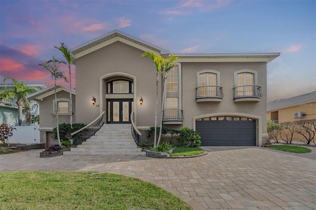 mediterranean / spanish home featuring french doors, an attached garage, a balcony, and stucco siding