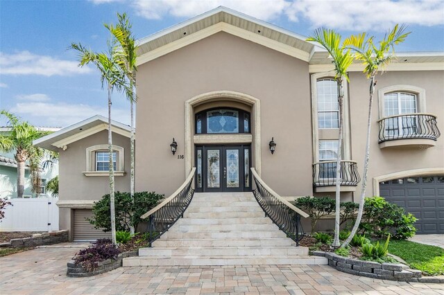 view of exterior entry with an attached garage, fence, decorative driveway, french doors, and stucco siding