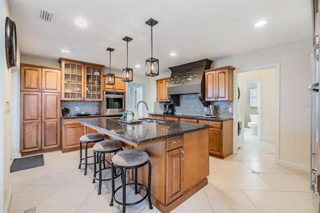 kitchen featuring brown cabinetry, a kitchen island with sink, and oven