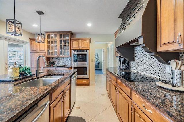 kitchen featuring light tile patterned floors, glass insert cabinets, appliances with stainless steel finishes, hanging light fixtures, and a sink