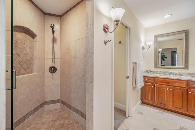 full bathroom featuring tile patterned flooring, a tile shower, vanity, and baseboards