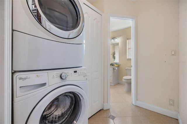 clothes washing area featuring light tile patterned floors, laundry area, stacked washing maching and dryer, and baseboards