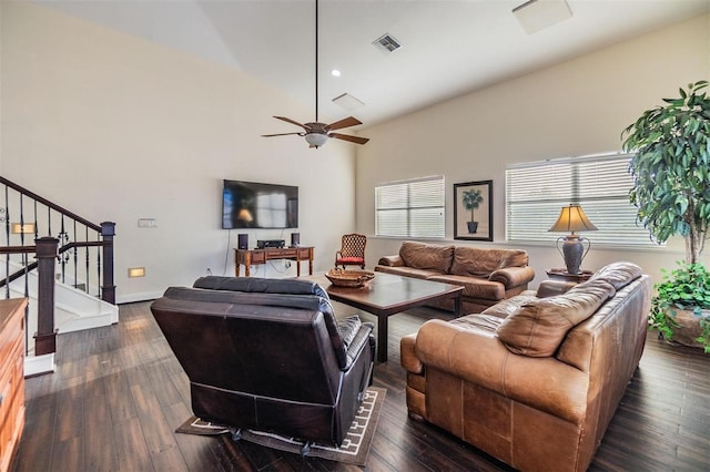 living area with ceiling fan, a towering ceiling, visible vents, stairs, and dark wood finished floors