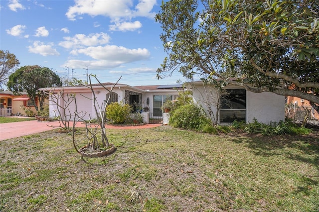 ranch-style home with solar panels, concrete driveway, a front yard, and stucco siding