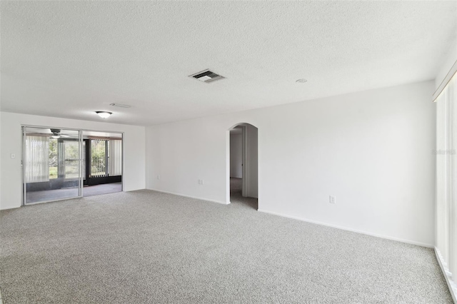 carpeted spare room featuring ceiling fan, visible vents, arched walkways, and a textured ceiling