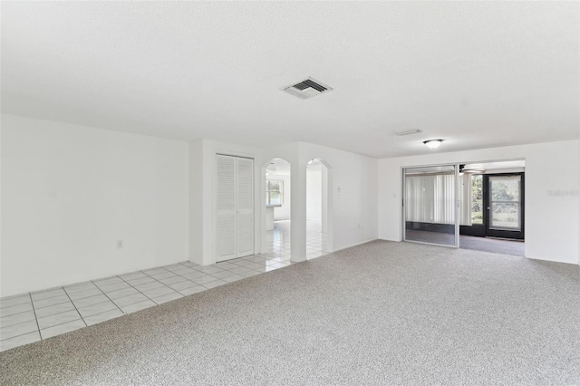 spare room with light carpet, light tile patterned floors, visible vents, arched walkways, and a textured ceiling