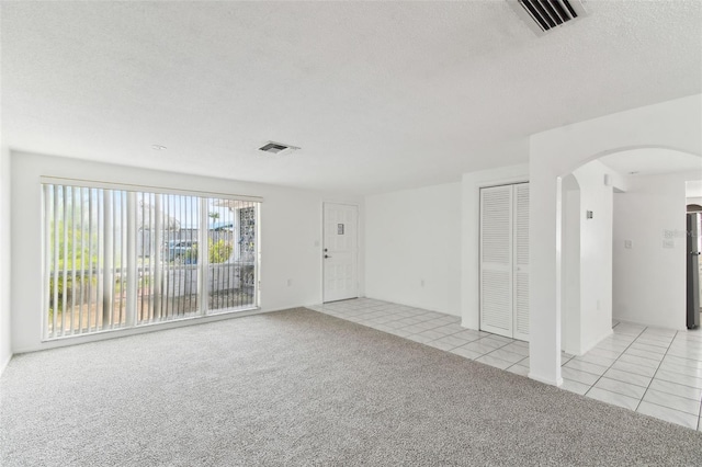 spare room featuring arched walkways, light tile patterned floors, a textured ceiling, light colored carpet, and visible vents