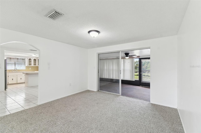 unfurnished bedroom with arched walkways, a textured ceiling, light tile patterned flooring, light colored carpet, and visible vents