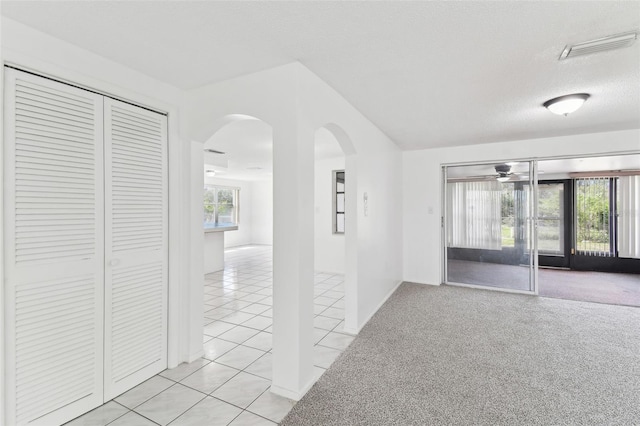 unfurnished room with arched walkways, light tile patterned floors, visible vents, light colored carpet, and a textured ceiling