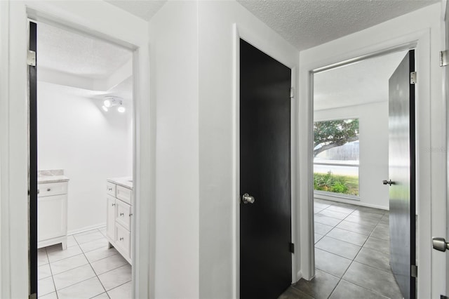 hallway with light tile patterned floors, a textured ceiling, and baseboards