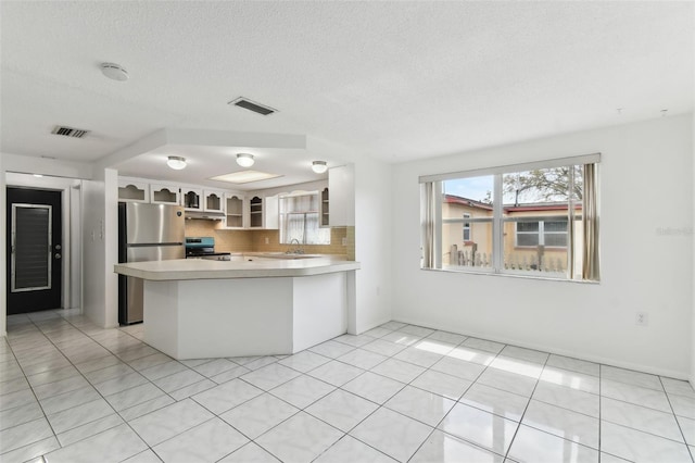 kitchen featuring stainless steel appliances, visible vents, light countertops, backsplash, and glass insert cabinets