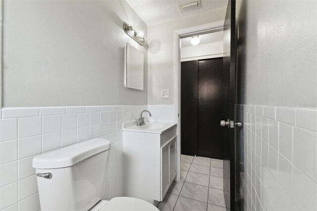 bathroom featuring a textured ceiling, toilet, visible vents, tile walls, and tile patterned floors