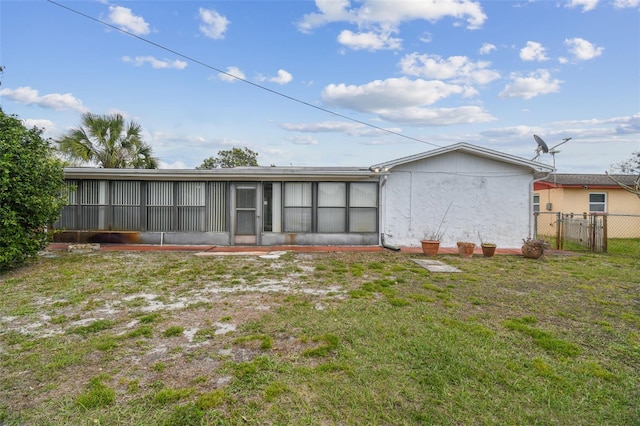 rear view of property featuring a lawn, fence, a sunroom, and stucco siding