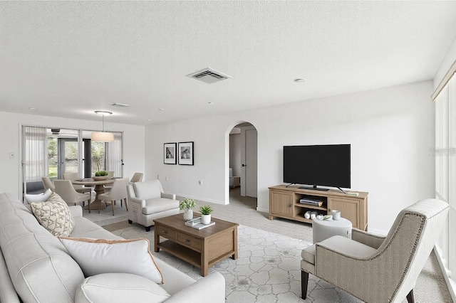 living room featuring light carpet, baseboards, visible vents, arched walkways, and a textured ceiling