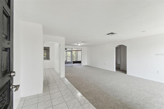 unfurnished room with arched walkways, light tile patterned floors, light colored carpet, visible vents, and a textured ceiling