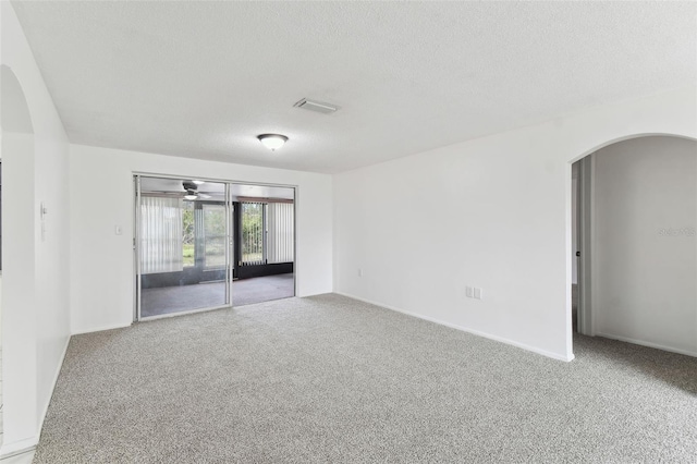 carpeted empty room featuring arched walkways, visible vents, ceiling fan, and a textured ceiling