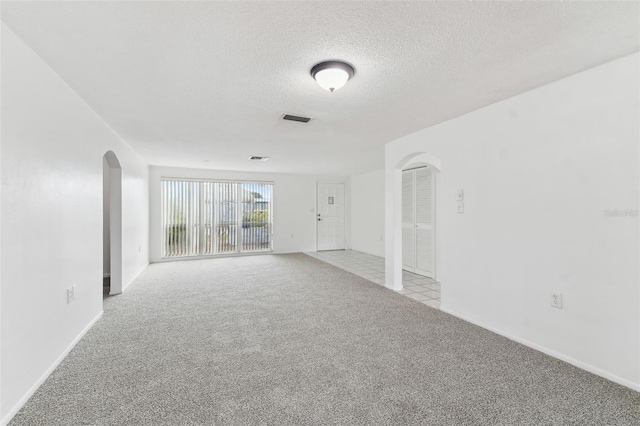 spare room with arched walkways, a textured ceiling, light colored carpet, visible vents, and baseboards