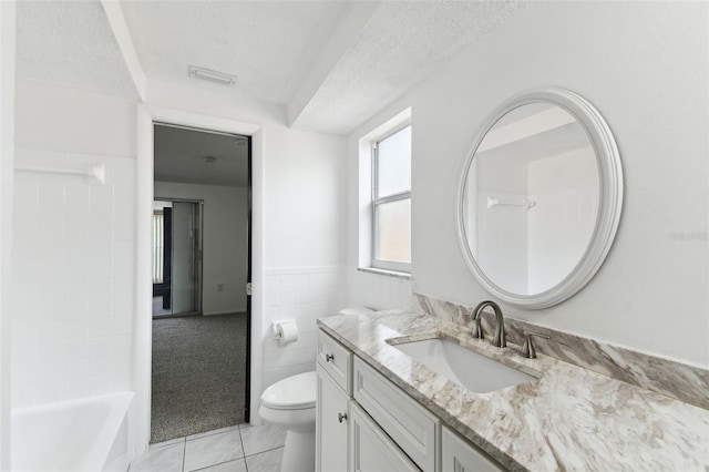 full bathroom with a textured ceiling, toilet, vanity, tile walls, and tile patterned floors