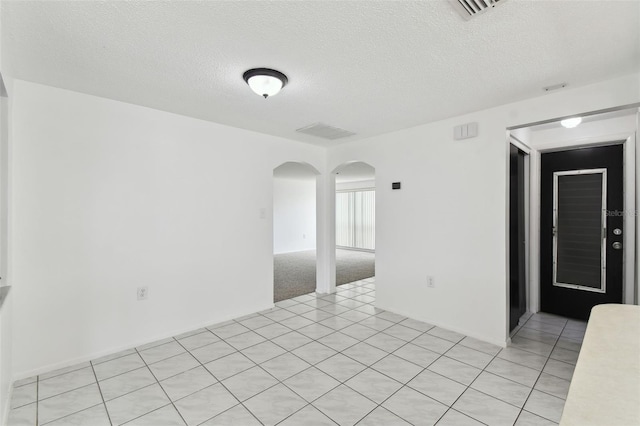 spare room featuring arched walkways, visible vents, a textured ceiling, and light tile patterned floors