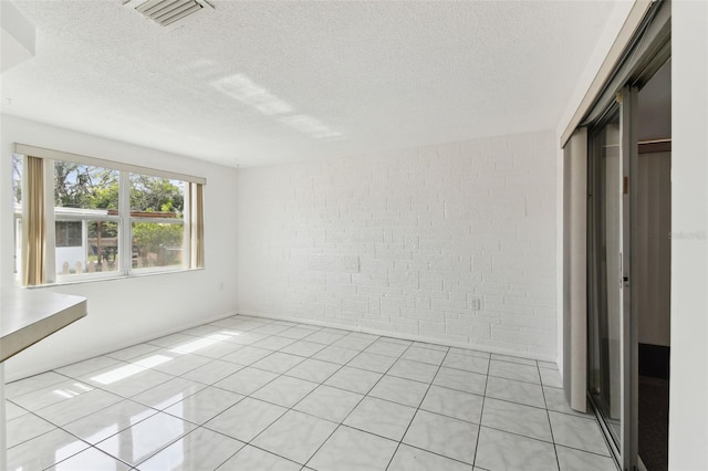 interior space with brick wall, visible vents, a textured ceiling, and light tile patterned flooring