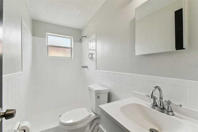 bathroom with a textured ceiling, toilet, vanity, tile walls, and a tile shower